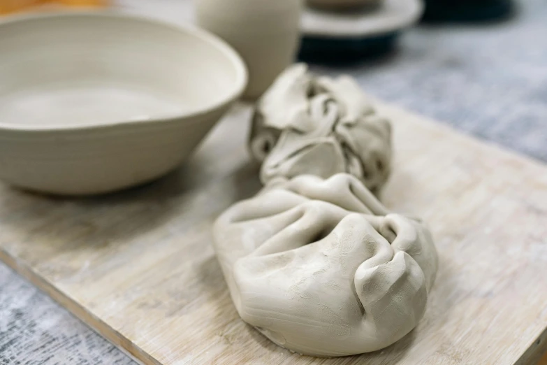 a couple of dumplings sitting on top of a wooden cutting board, a marble sculpture, inspired by Sarah Lucas, process art, white clay, grey, pot, medium close up