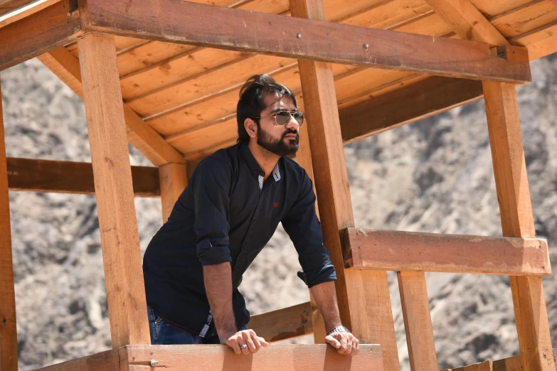 a man standing on top of a wooden structure, inspired by Jitish Kallat, pexels contest winner, plein air, a portrait of rahul kohli, avatar image, profile picture, an arab standing watching over