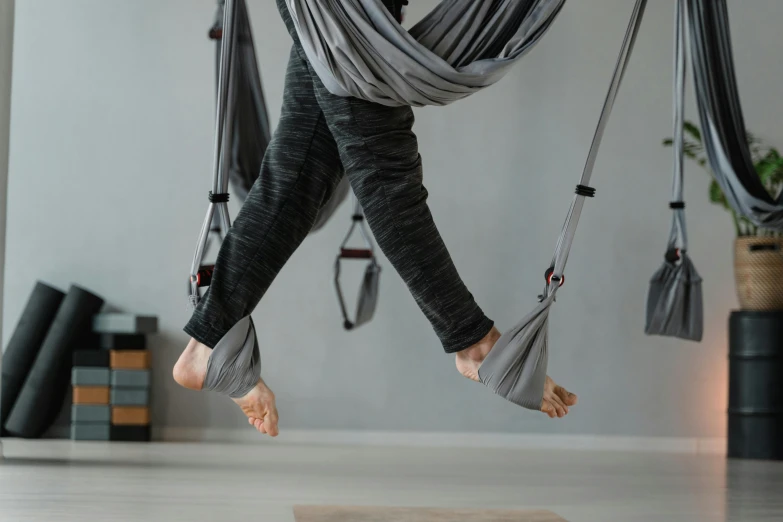 a woman flying through the air in a hammock, by Emma Andijewska, trending on pexels, arabesque, grey and silver, local gym, in a jumping float pose, two hang