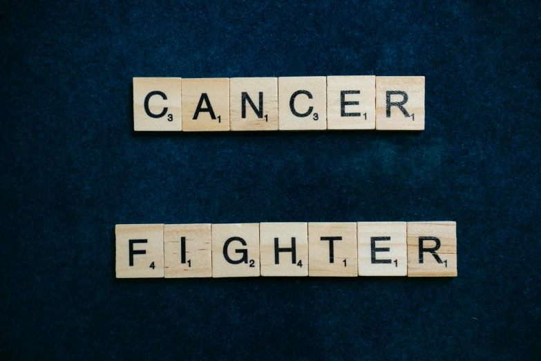 two scrabbles spelling cancer and fighter on a blue background, by Caroline Mytinger, pexels contest winner, human fighter, background image, on black background, a wooden