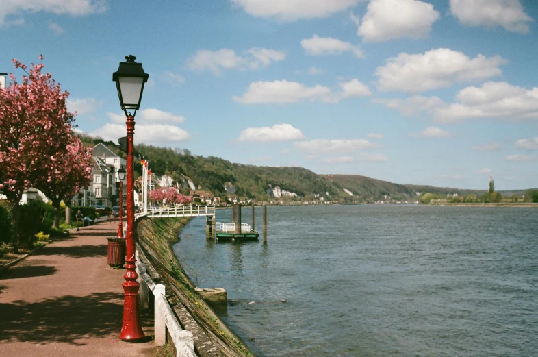 a street light sitting next to a body of water, a picture, inspired by Richmond Barthé, pexels contest winner, scenic view of river, liege, sunny sky, gas lanterns