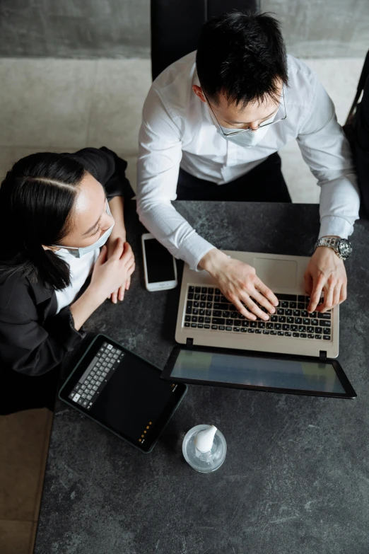 a couple of people sitting at a table with a laptop, in front of a computer