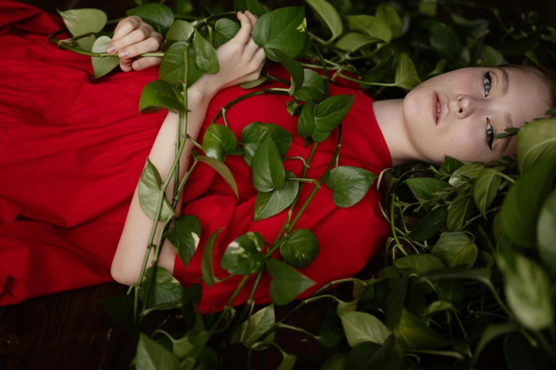 a woman in a red dress laying on a bed of leaves, inspired by Elsa Bleda, magic realism, overgrown ivy plants, greta thunberg, ignant, red shirt