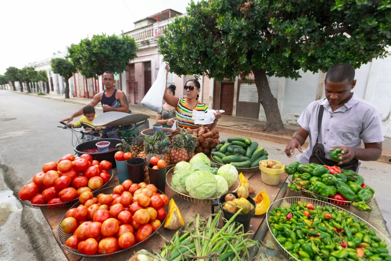 a group of people standing around a table full of fruits and vegetables, by Ceferí Olivé, cuba, square, tourism, street corner