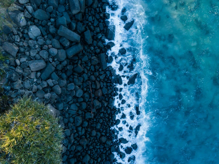 a large body of water next to a lush green hillside, an album cover, by Daniel Lieske, pexels contest winner, black sand, close-up from above, half blue, half and half