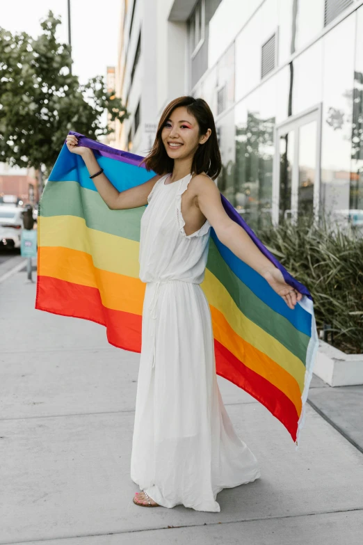 a woman in a white dress holding a rainbow flag, inspired by helen huang, wearing a long flowy fabric, pokimane, wearing a scarf, jc park