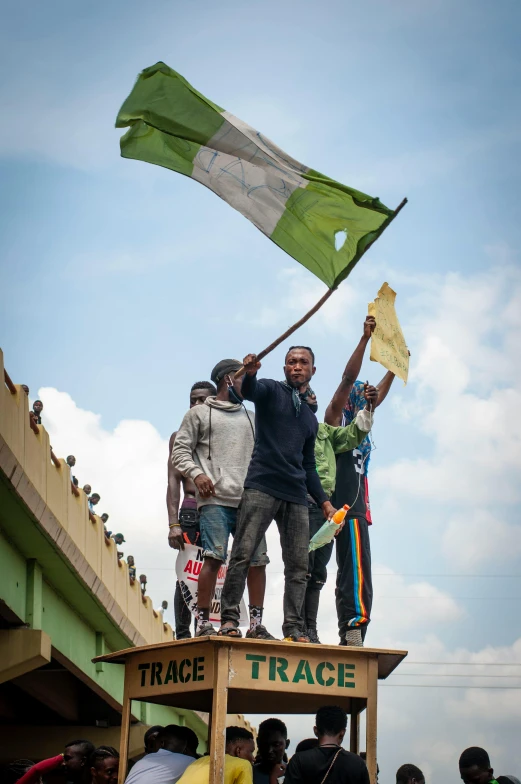 a group of people standing on top of a wooden cart, by Ingrida Kadaka, flickr, happening, green flag, waving, standing on rooftop, unmistakably kenyan