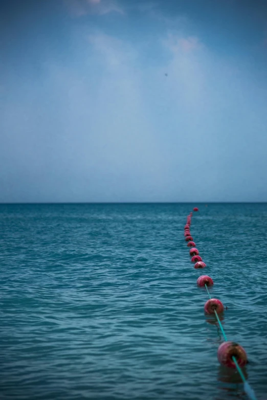 a row of buoys sitting on top of a body of water, an album cover, unsplash, red sea, cords, long view, varadero beach