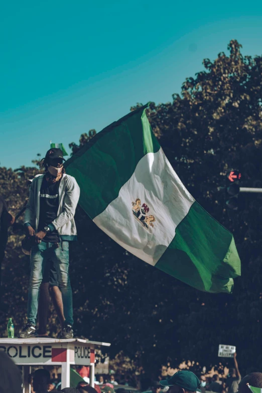 a man standing on top of a truck holding a flag, by Bernardino Mei, pexels contest winner, symbolism, irish youtuber, green and white, teenage, 🚿🗝📝