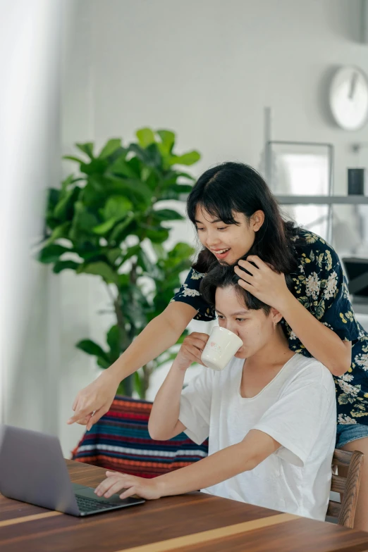 a man and woman sitting at a table with a laptop, by Reuben Tam, pexels contest winner, woman holding another woman, milk, playful, asian decent
