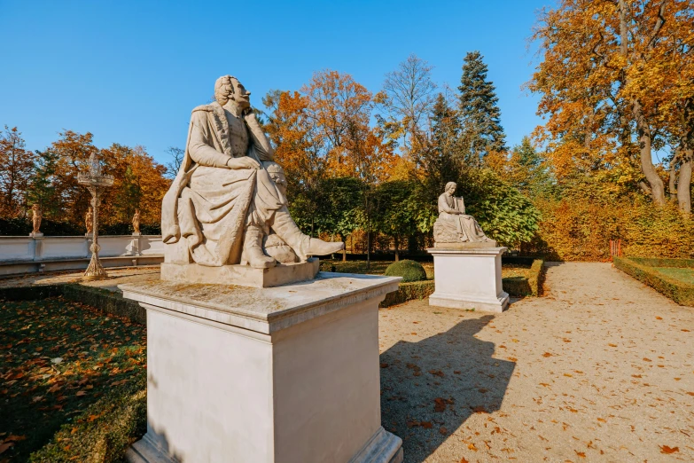 a couple of statues sitting next to each other, a marble sculpture, inspired by Gyula Aggházy, neoclassicism, in autumn, lush surroundings, in the sun, during autumn