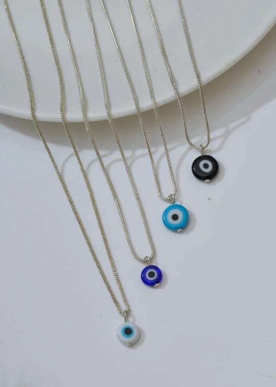 four evil eye necklaces on a white plate, zoomed in, blue silver and black, kami, detailed product image