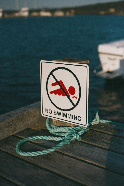 a no swimming sign sitting on top of a wooden dock, unsplash, graffiti, people swimming, subreddit / r / whale, no - text no - logo, summer swimming party