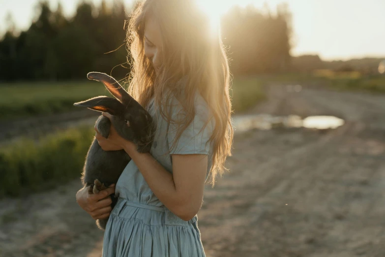 a woman holding a rabbit on a dirt road, by Emma Andijewska, pexels contest winner, evening sunlight, handsome girl, grey, 15081959 21121991 01012000 4k