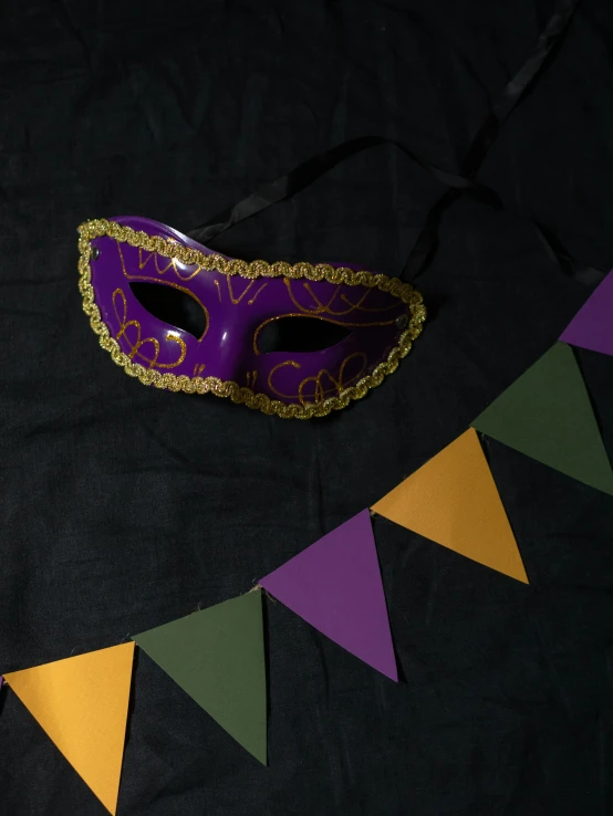 a purple mask sitting on top of a black table, inspired by Mardi Barrie, banners, green and gold, low quality photo, flatlay