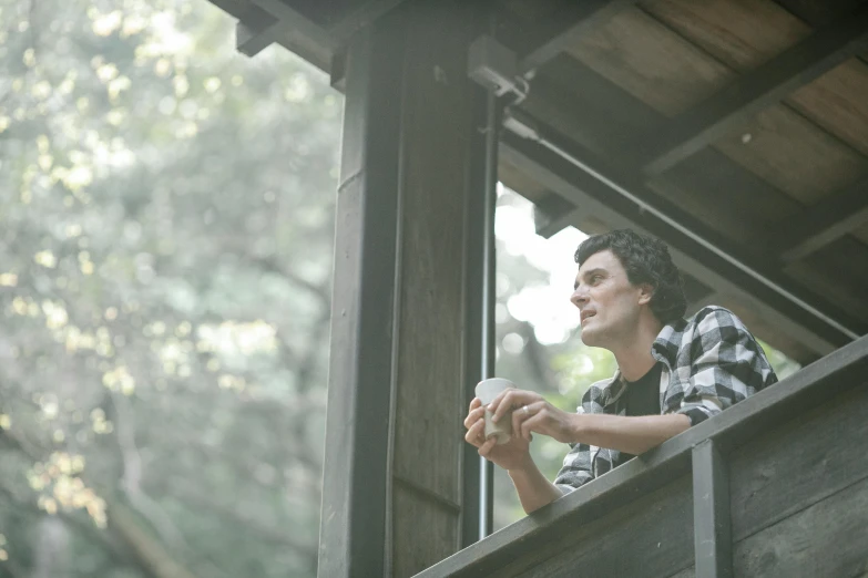 a man sitting on a balcony with a cup of coffee, adam ondra, cabin in the woods, profile image, high resolution film still