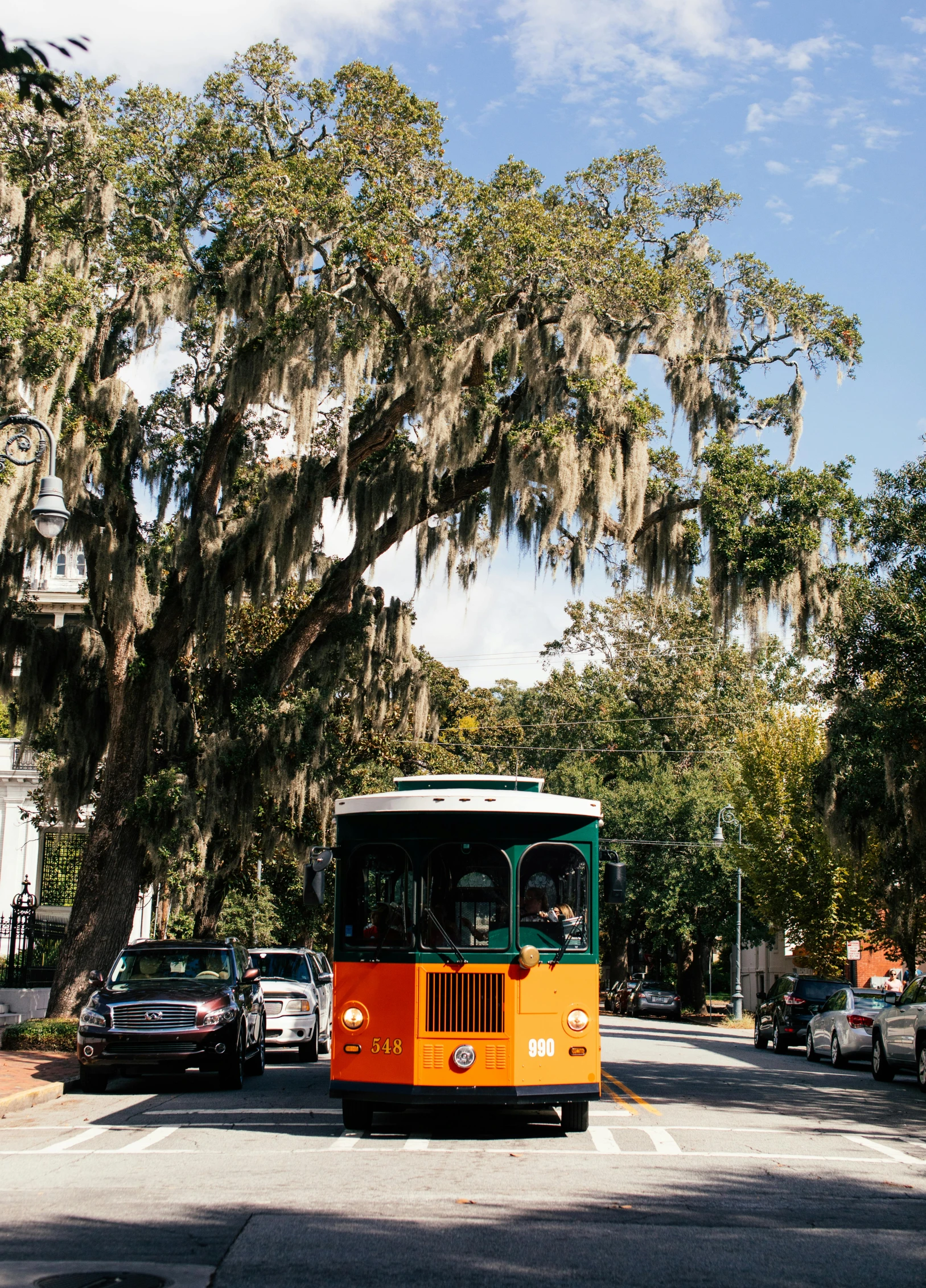 an orange and green bus driving down a street, spanish moss, square, ignant, preserved historical