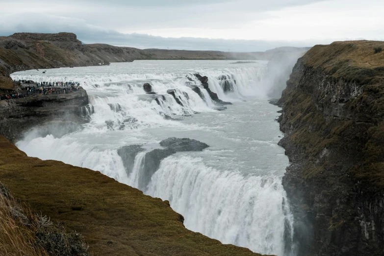 a group of people standing at the base of a waterfall, by Hallsteinn Sigurðsson, pexels contest winner, hurufiyya, whirlpool, grey, distant photo, national geohraphic