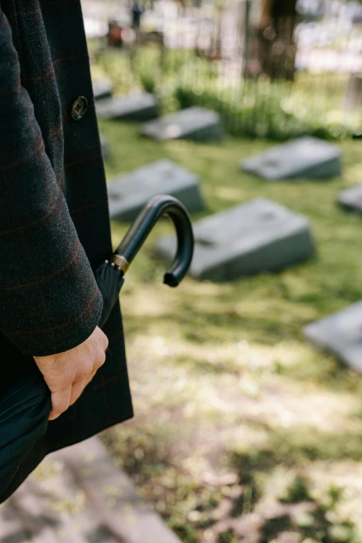 a person holding an umbrella in a cemetery, holding a cane, profile image