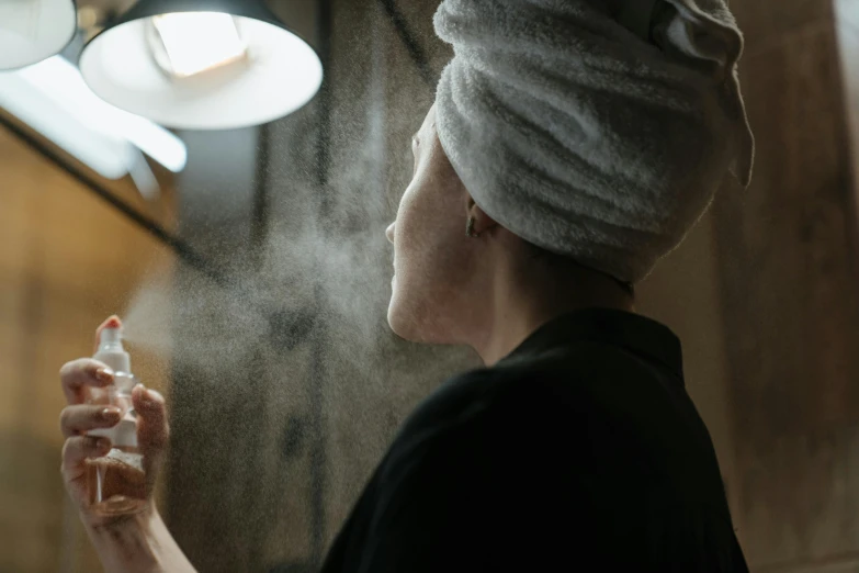 a woman with a towel on her head spraying water on her face, inspired by Elsa Bleda, pexels contest winner, dry brushing, facing away, emerging from her lamp, skincare
