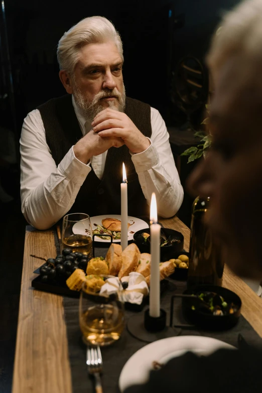 a man sitting at a table with a plate of food, by Jesper Knudsen, pexels contest winner, renaissance, white candles, old gigachad with grey beard, ( ( theatrical ) ), romantic