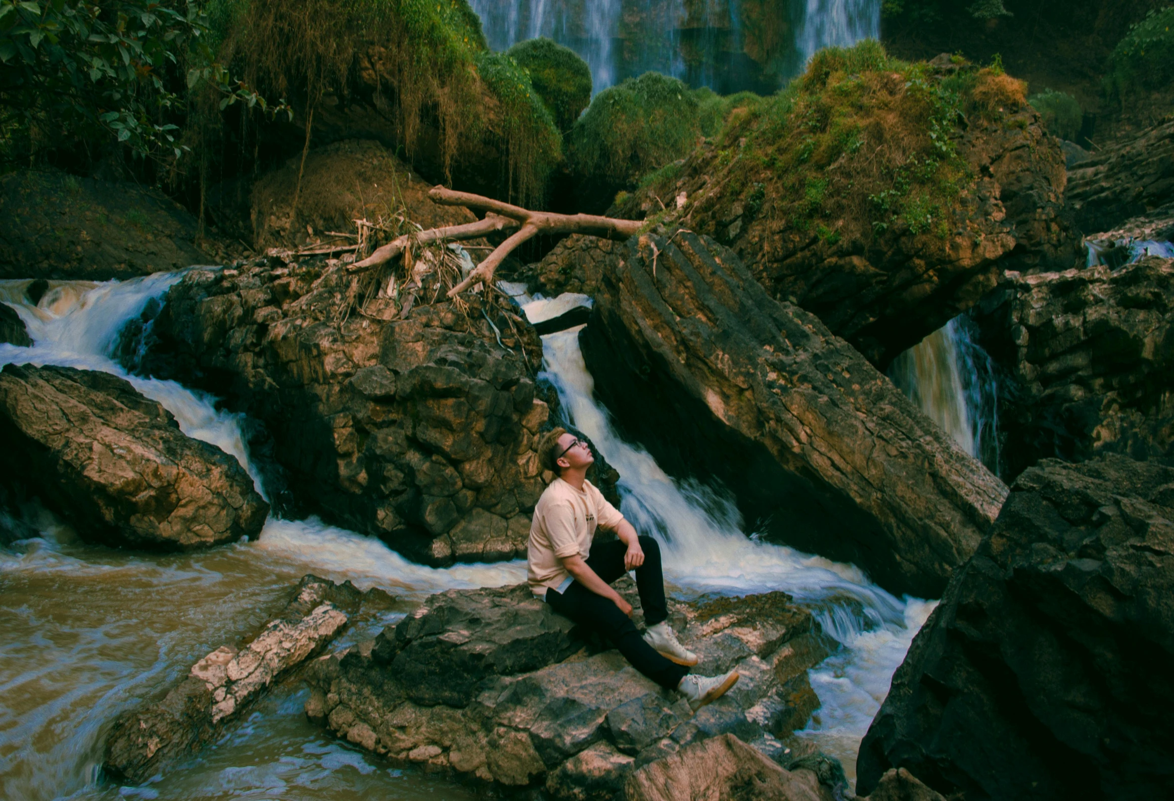 a man sitting on a rock in front of a waterfall, an album cover, by Elsa Bleda, unsplash, ilya golitsyn, post malone, ignant, julian ope