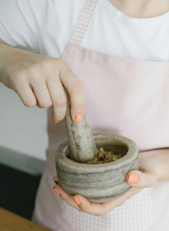a close up of a person holding a mortar and a bowl, inspired by Ruth Jên, trending on pexels, wearing an apron, made of cement, detailed product image, profile picture