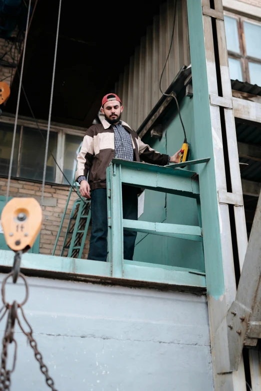 a man standing on the balcony of a building, in a workshop, real life photo of a syrian man, egor letov, opposite the lift-shaft