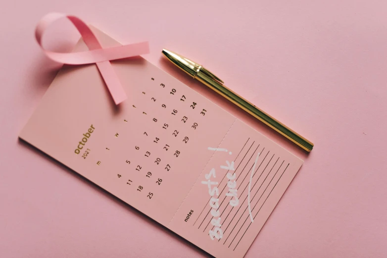 a pen sitting on top of a calendar next to a pink ribbon, trending on pexels, gold foil, surgical supplies, thumbnail, pink skin