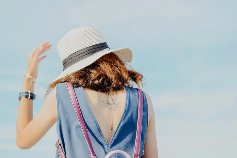 a woman standing on top of a sandy beach, a tattoo, trending on pexels, blue fedora, from back, background image, blue and pink