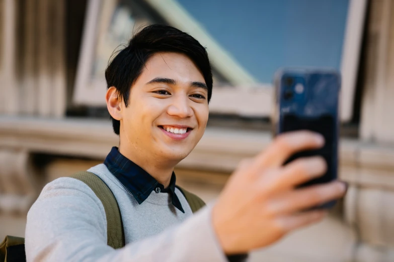 a man taking a selfie in front of a building, inspired by Reuben Tam, trending on pexels, realism, young cute wan asian face, student, friendly smile, profile picture 1024px