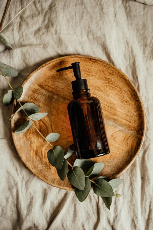 a bottle of liquid sitting on top of a wooden plate, pexels contest winner, renaissance, skincare, eucalyptus, thumbnail, brown