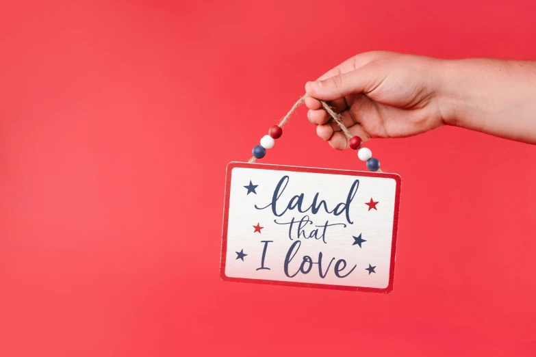 a hand holding a sign that says land that i love, red white background, ornament, background image, vibrant threads