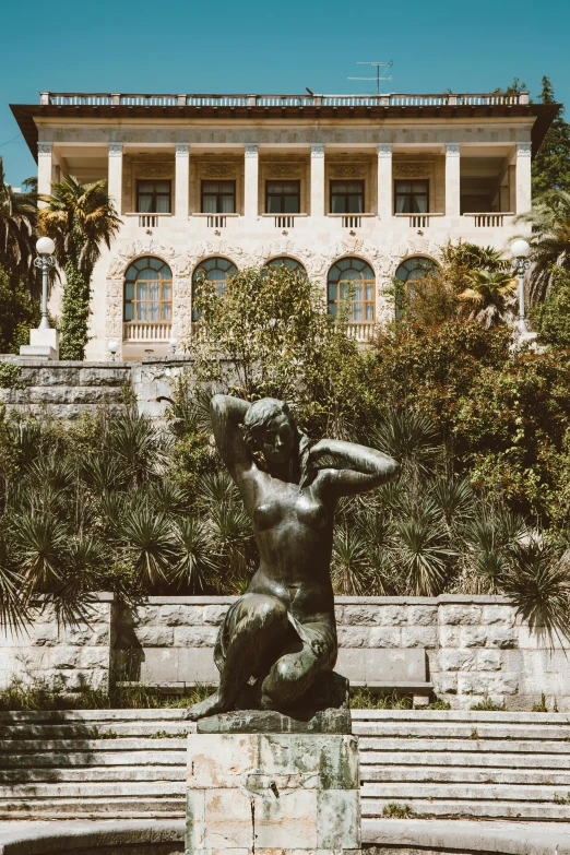 a statue of a woman in front of a building, inspired by Aristide Maillol, lake view, split near the left, lush surroundings, manufactured in the 1920s