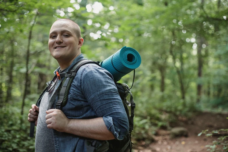 a man with a blue yoga mat on his back, by Meredith Dillman, pexels contest winner, forest in the background, big smirk, slightly overweight, caleb from critical role