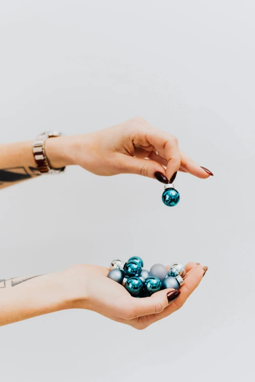 a woman holding a christmas ornament in her hands, a colorized photo, by Nicolette Macnamara, trending on unsplash, minimalism, made of liquid metal and marble, cannonballs, blue gray, many pieces