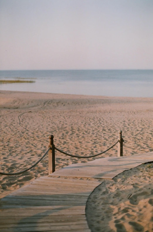 a bench sitting on top of a sandy beach next to the ocean, kodak portra, rope bridges, summer evening, runway