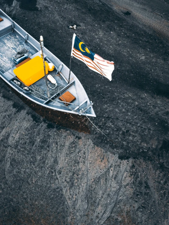a boat sitting on top of a beach next to an american flag, a photo, inspired by Chesley Bonestell, pexels contest winner, hurufiyya, black sand, malaysian, mars aerial photography, charcoal and yellow leather