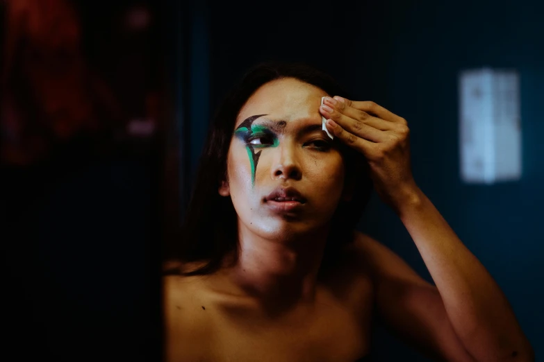 a woman is putting makeup on her face, trending on pexels, hyperrealism, body paint, androgynous male, oil slick, looking sad