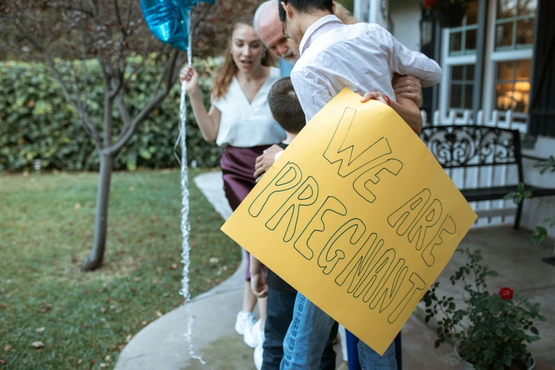 a couple of people that are holding a sign, by Julia Pishtar, pexels, happening, pregnancy, presents, a person standing in front of a, welcoming