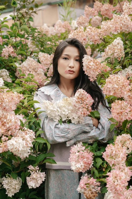 a woman standing in front of a bush of flowers, an album cover, inspired by Jung Park, gemma chan beautiful girl, medium format, lucy liu portrait, hydrangea