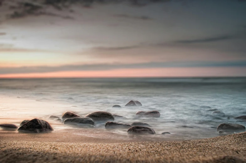 a group of rocks sitting on top of a sandy beach, unsplash, tonalism, slow exposure hdr 8 k, hazy water, ((rocks))