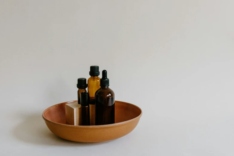 a wooden bowl filled with bottles of essential oils, a still life, inspired by Ceferí Olivé, unsplash, minimalist photo, terracotta, miniature product photo, full body image