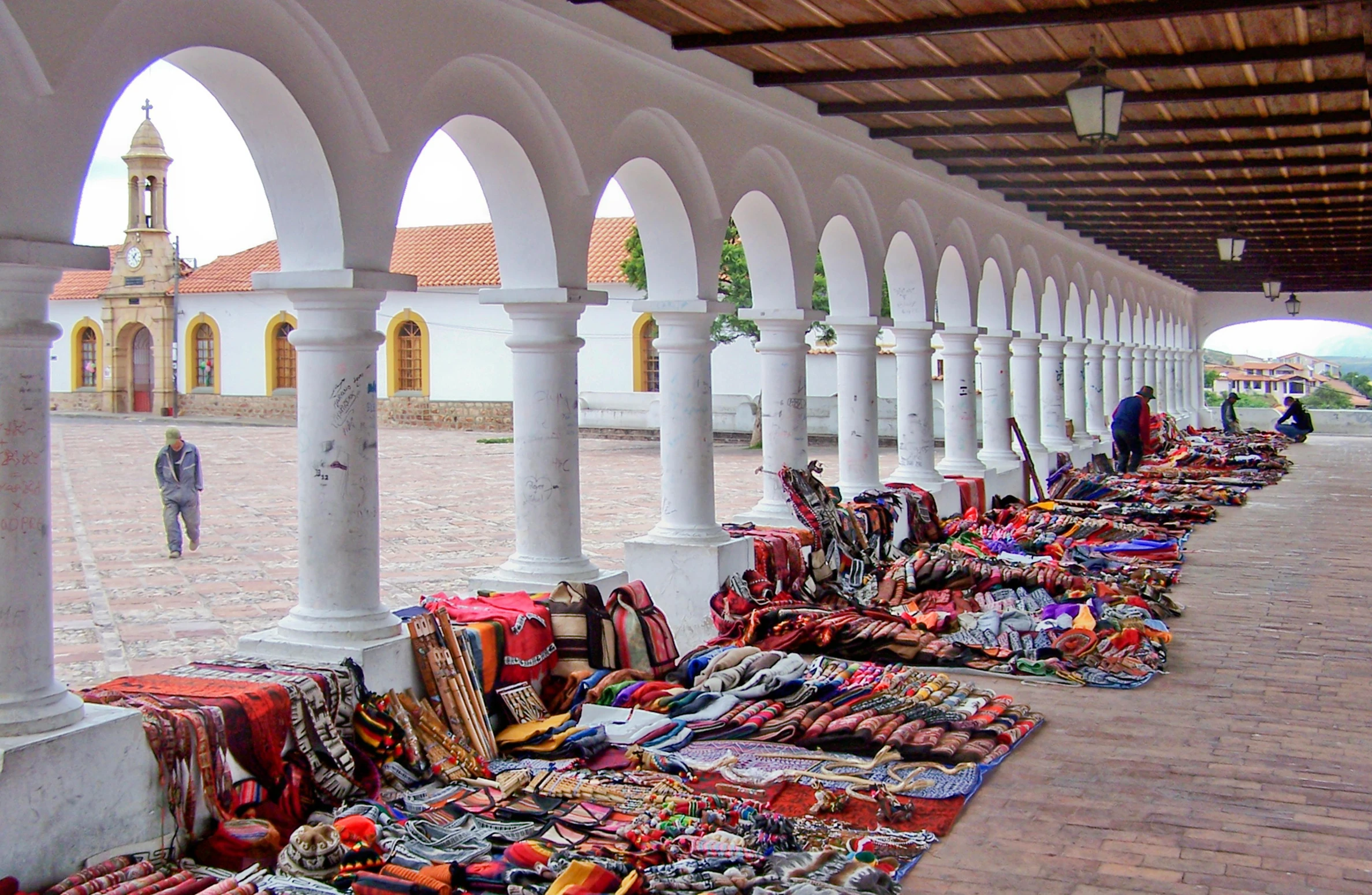 a row of rugs sitting on top of a brick floor, by Carey Morris, trending on unsplash, quito school, white buildings with red roofs, presenting wares, arches adorned pillars, taken in the late 2000s