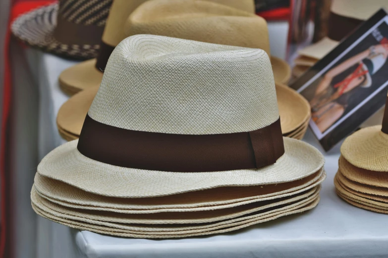 a bunch of hats sitting on top of a table, an album cover, by Thomas Häfner, unsplash, arts and crafts movement, brown and cream color scheme, sri lanka, fedora, trimmed with a white stripe