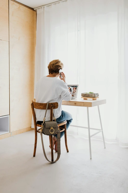 a woman sitting at a desk talking on a cell phone, by Jan Tengnagel, minimalism, wooden side table, fancy apartment, dwell, hanging