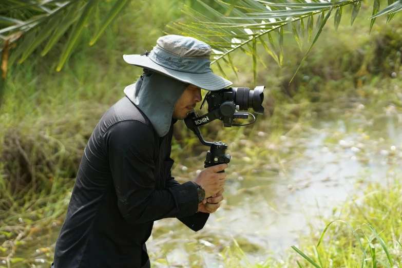 a man that is standing in the grass with a camera, unsplash, sumatraism, still from nature documentary, wearing adventure gear, neoprene, in an action pose