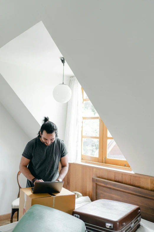 a man sitting on top of a bed in a room, trending on unsplash, light and space, working on her laptop, slanted ceiling, document photo, dwell