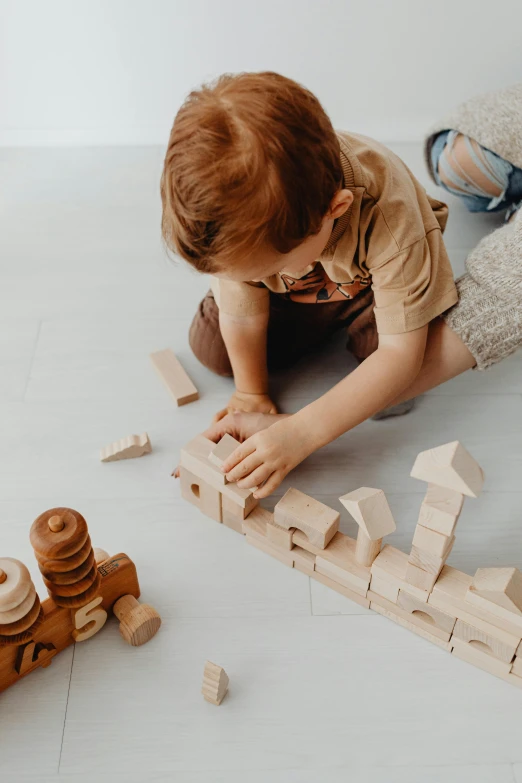 a little boy playing with wooden blocks on the floor, pexels contest winner, oversized enginee, plain background, thumbnail, small