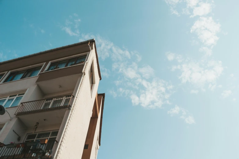 a tall building with a balcony and balconies, a photo, pexels contest winner, sunny clear sky, uniform off - white sky, standing outside a house, view from the ground